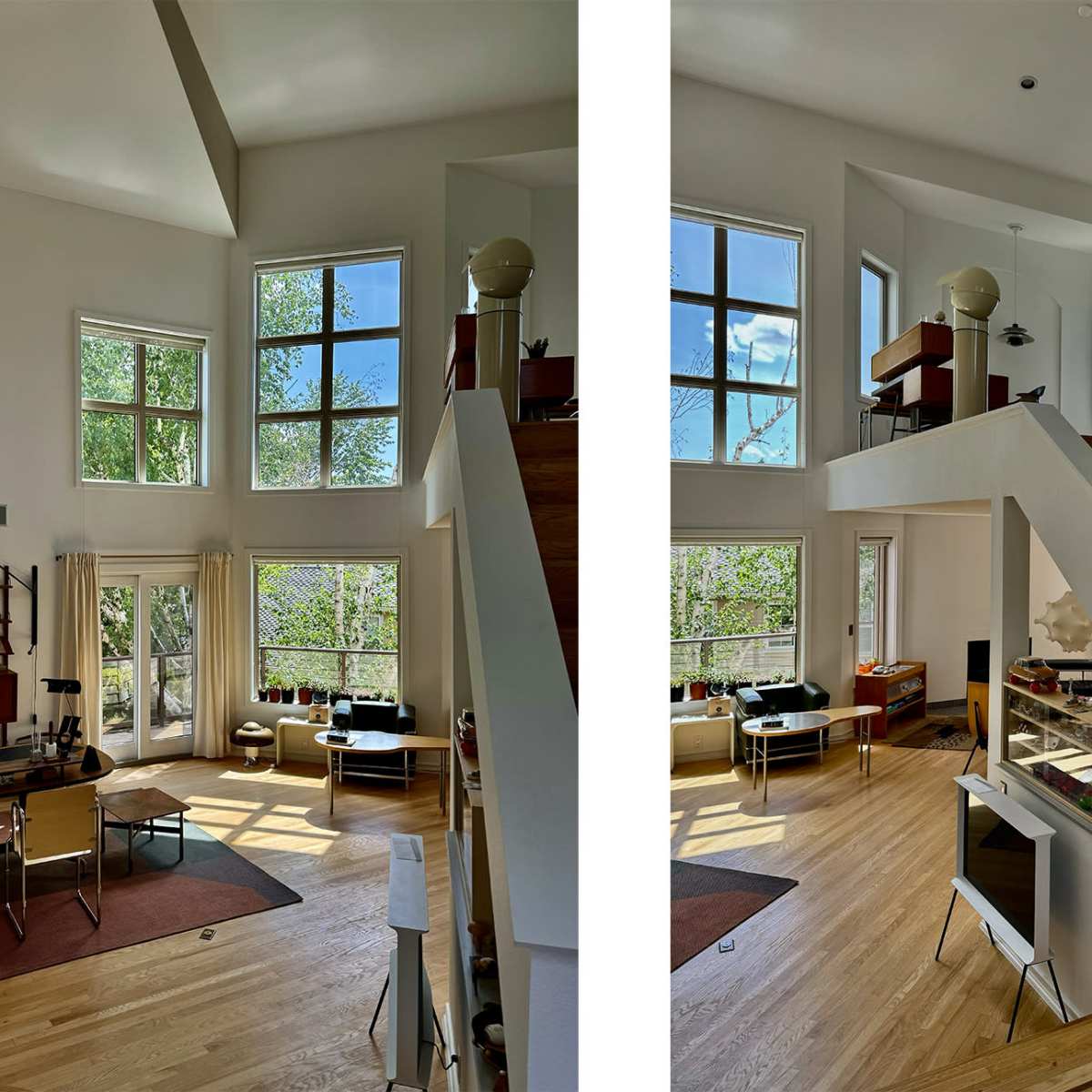 A spacious interior of a modern home with large windows, wooden stairs, and a view of greenery outside.