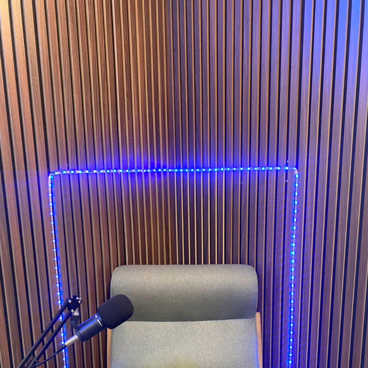 A microphone beside a gray chair framed by blue LED lights against a wooden paneled wall.