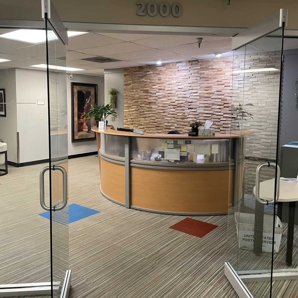 A reception area with a curved front desk, a stone wall backdrop, and a clear glass entrance.