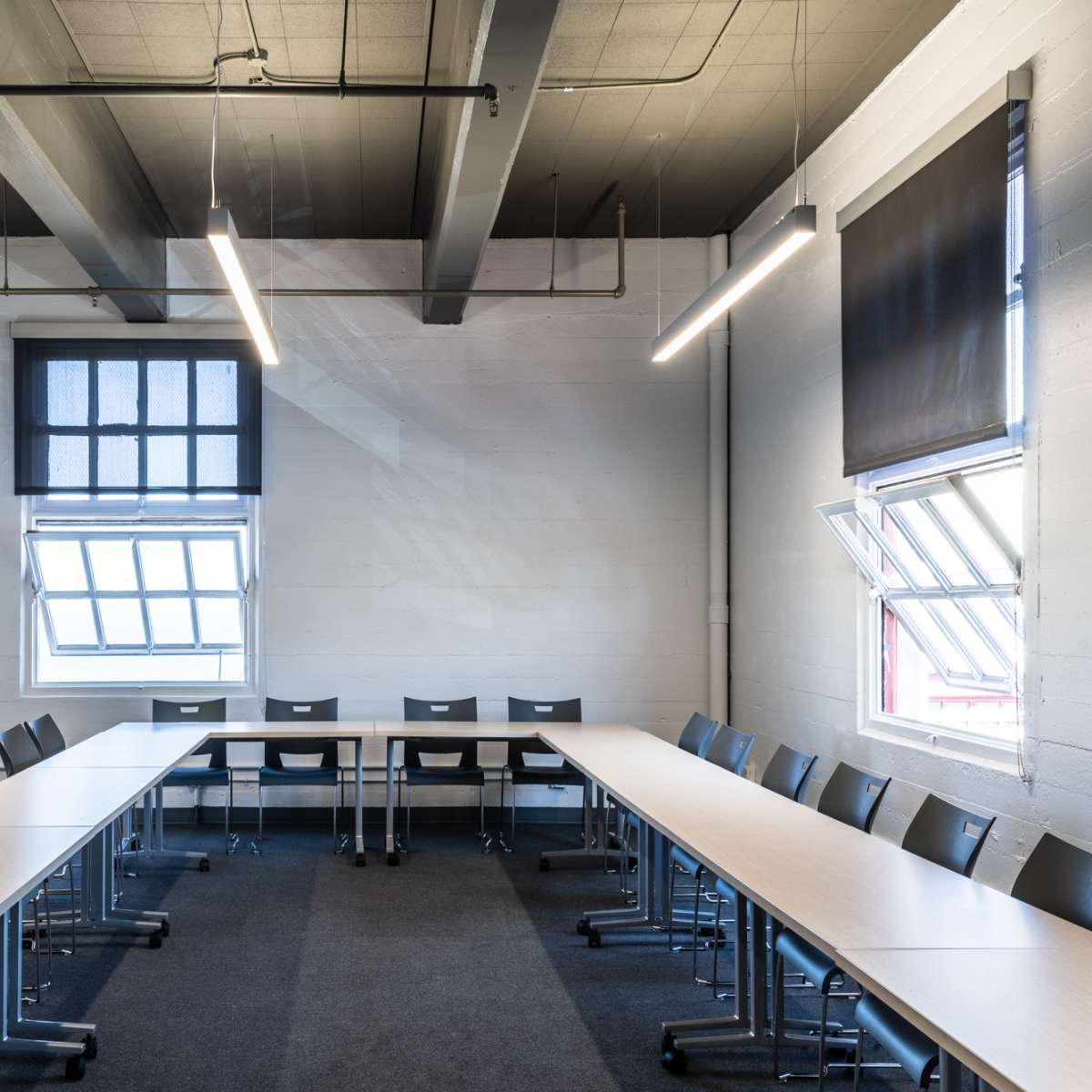 A spacious conference room with a large U-shaped table surrounded by modern black chairs and two windows.