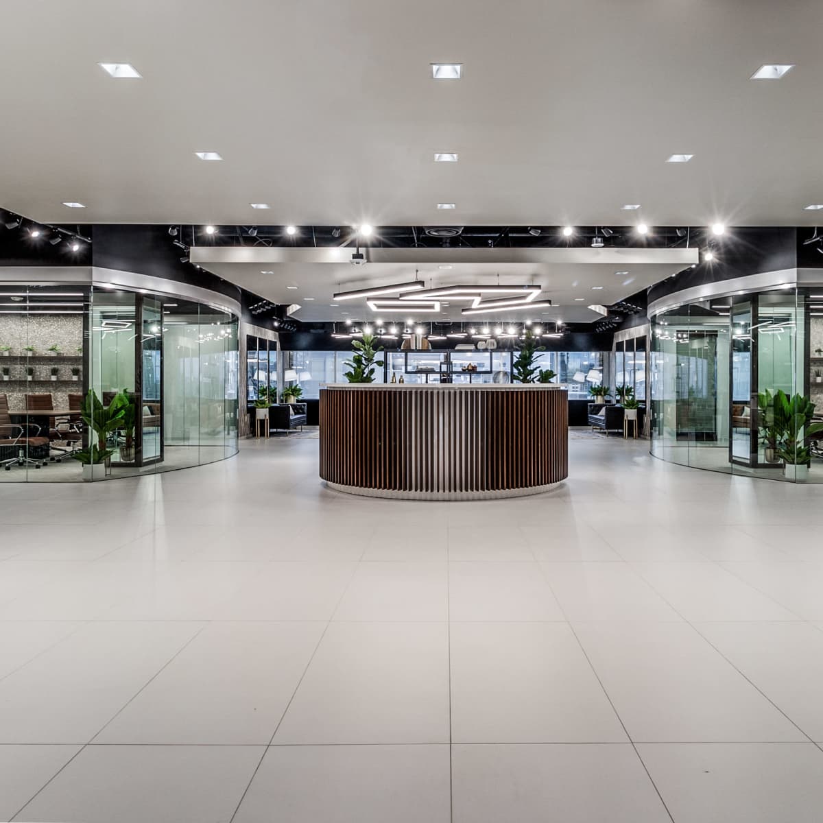 A modern office lobby with a circular reception desk surrounded by glass meeting rooms and a large open workspace.