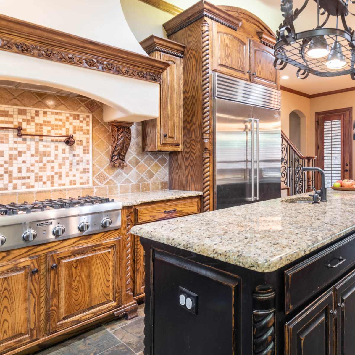 A kitchen with wooden cabinetry, a granite island, stainless steel appliances, and a dining area with a wooden table and chairs.