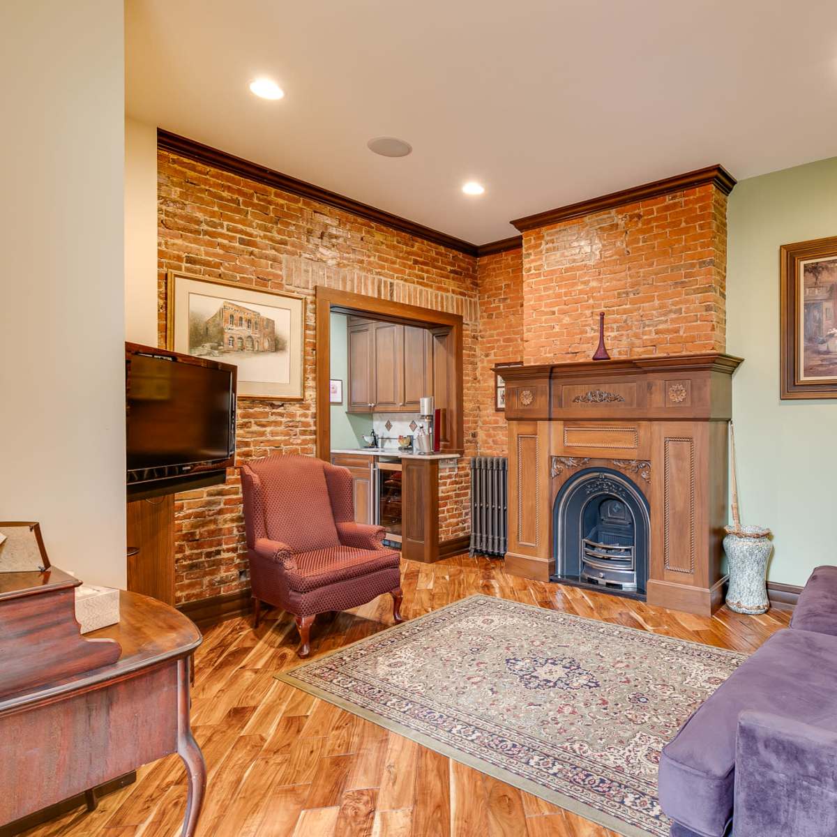 A cozy living room featuring a brick accent wall, a wooden fireplace, a purple sofa, and a wooden chair, with a decorative rug on the floor.