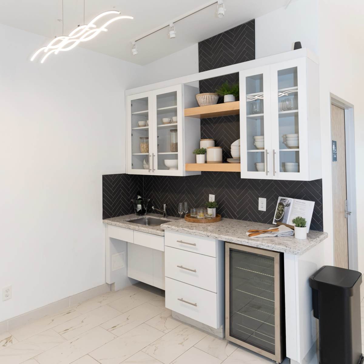A modern kitchen corner with white cabinetry, a granite countertop, a small sink, a wine fridge, and a decorative backsplash.