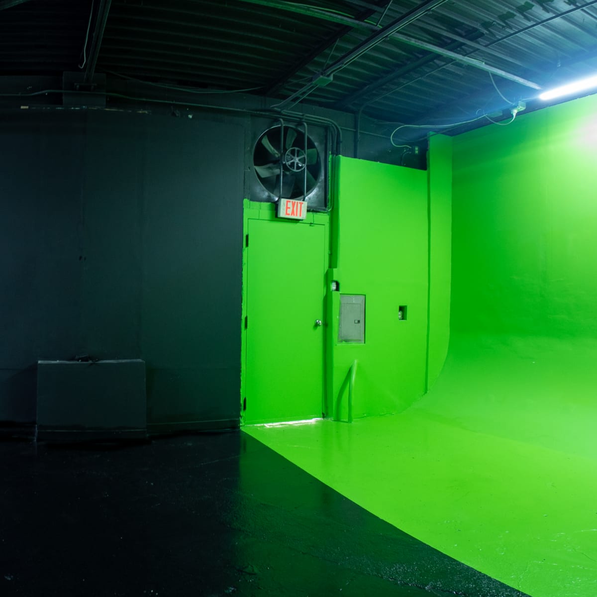 A studio space featuring a black wall with a green-painted corner, a closed rolling door, and contrasting black and white flooring.