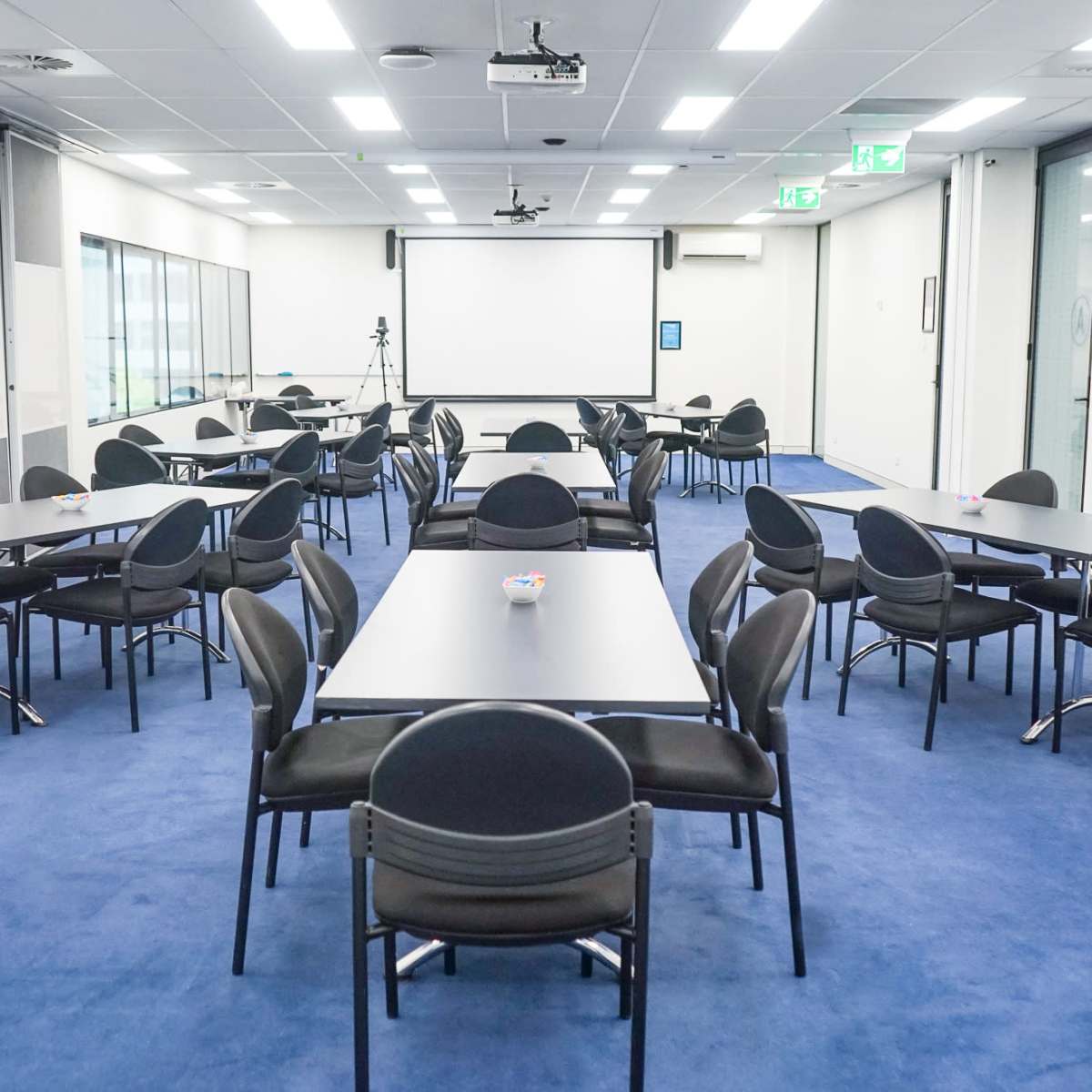 A professional meeting room with multiple tables and chairs arranged in a clean, organized layout on a blue carpet.