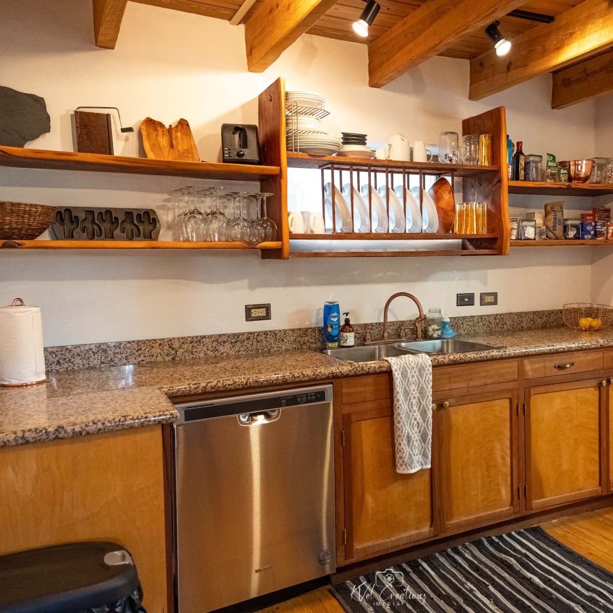 A kitchen with wooden shelves displaying dishes and glasses, a granite countertop, and appliances including a dishwasher.