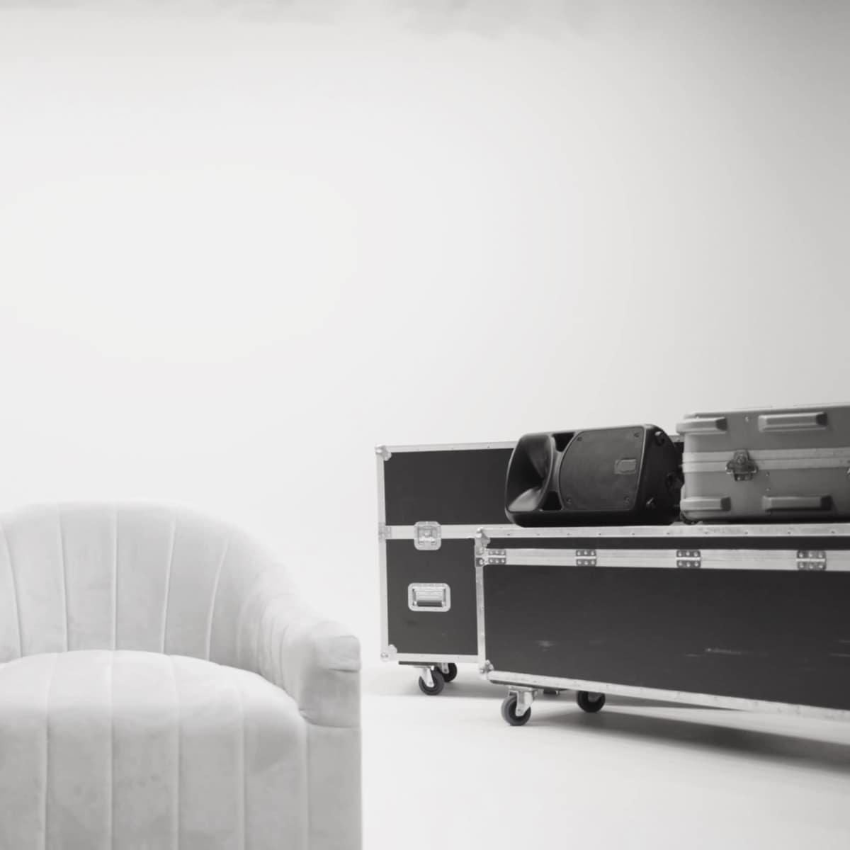 A white upholstered chair is positioned between two black equipment cases on a minimal white background.