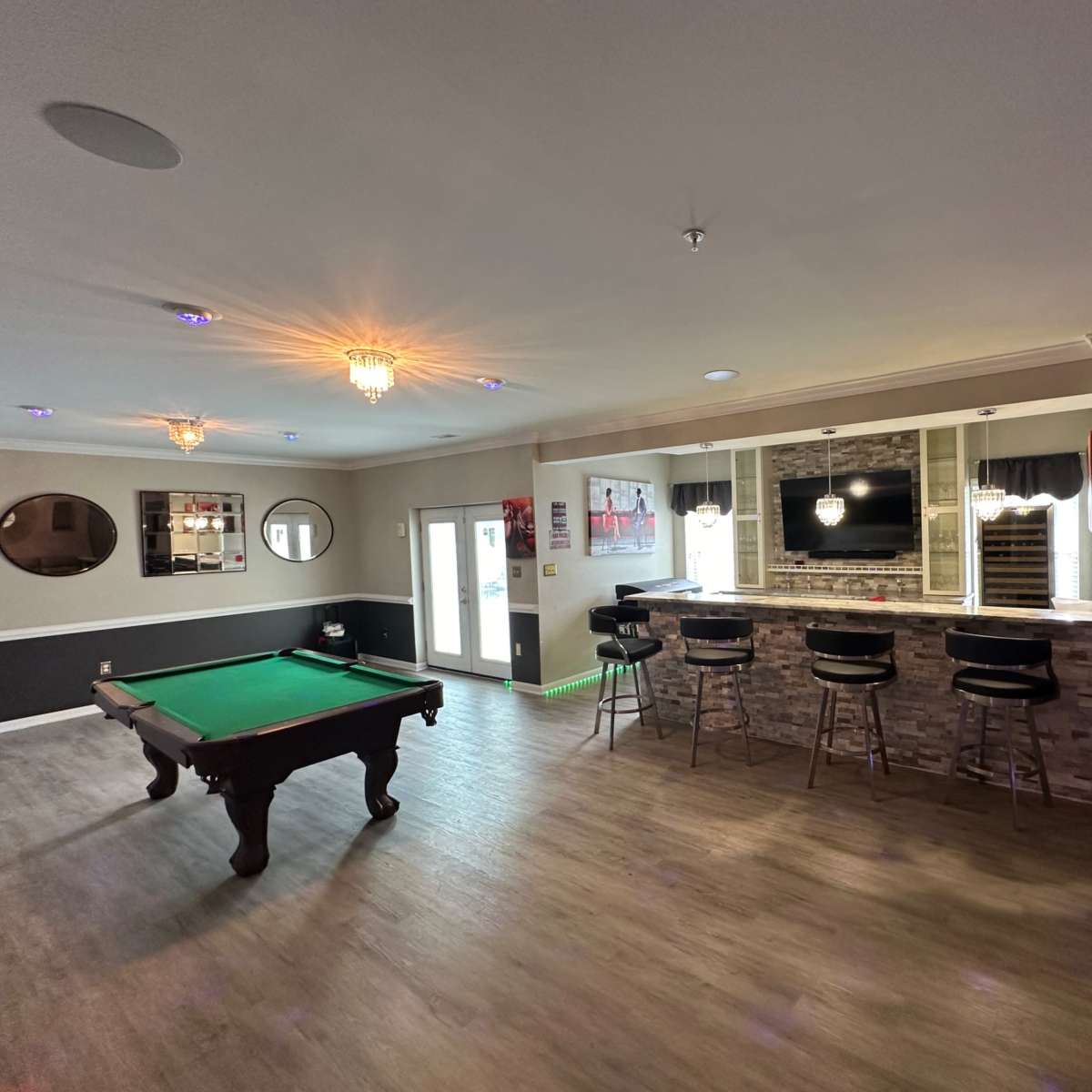 A spacious game room featuring a pool table, a bar area with high stools, and a television mounted above a stone accent wall.