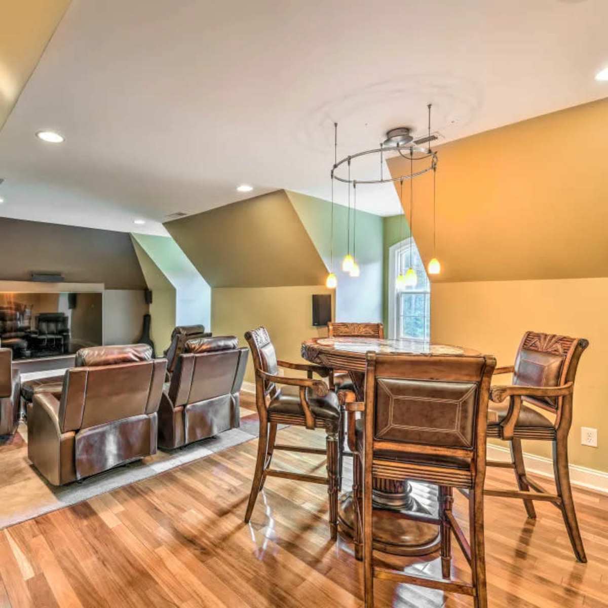 A spacious attic room with a seating area, dining table, and large windows.