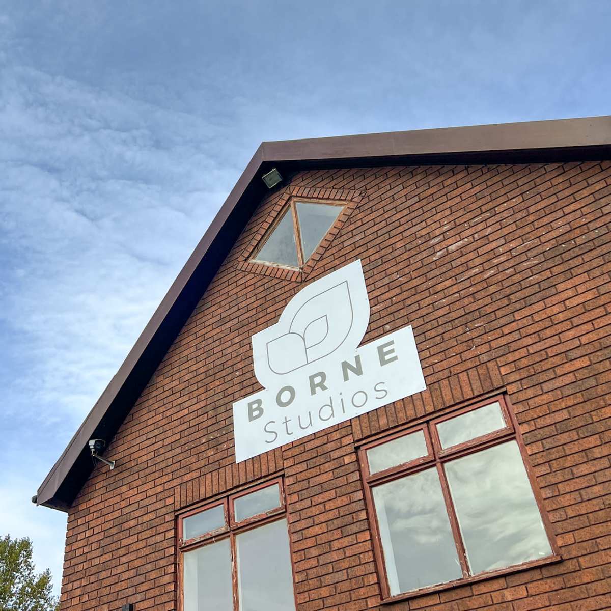 A red brick building with a sign that reads "BORNE Studios" beneath a cloudy blue sky.