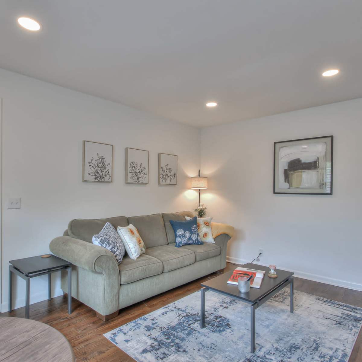 A modern living room features a green sofa, a coffee table, and artwork on the walls, with warm lighting and hardwood floors.