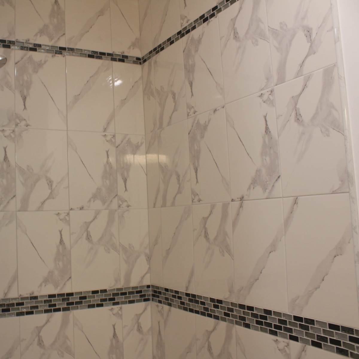 A modern tiled shower with gray and white marbled tiles and a mosaic border.