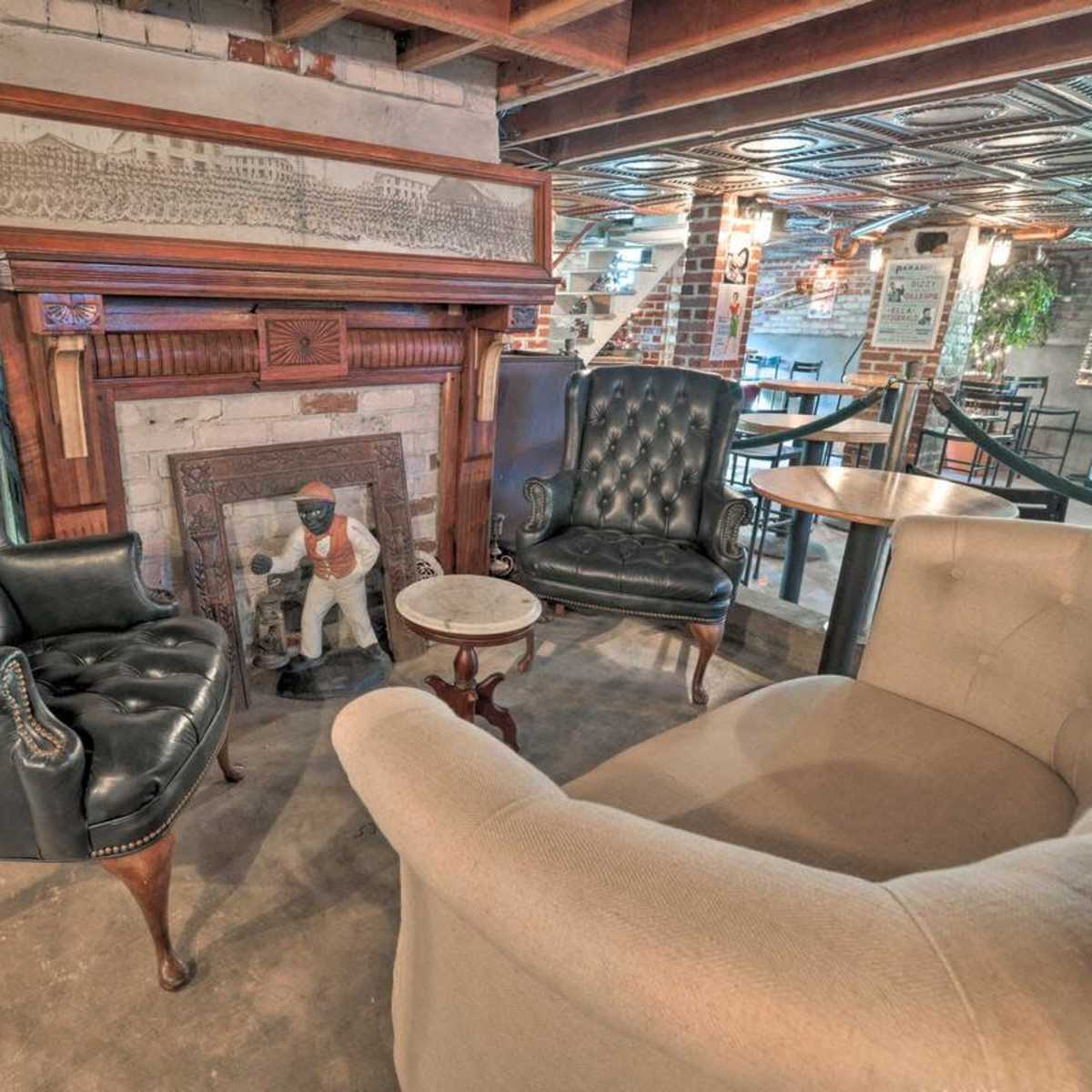 A cozy seating area with two leather armchairs and a light-colored sofa arranged around a small table in front of a decorative fireplace featuring an ornate mantel and a statue.