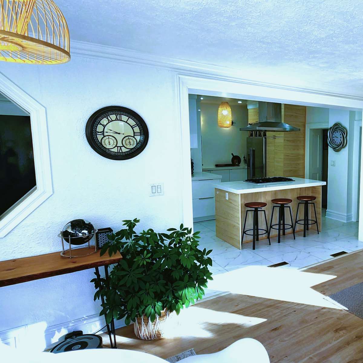 A bright living room that connects to a kitchen, featuring modern furniture, a large television, and plants.