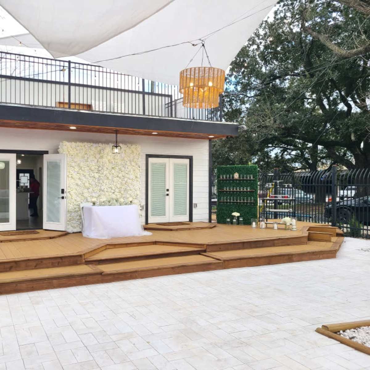A spacious outdoor deck area with a stage, surrounded by greenery and a modern building featuring large windows and a decorative wall.