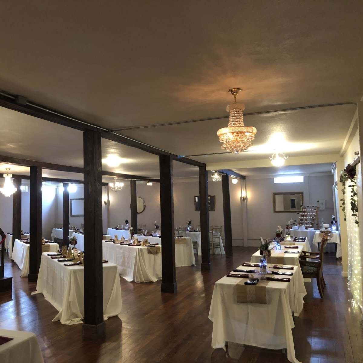 A spacious banquet hall with neatly arranged tables covered in white tablecloths and a staircase in the background.