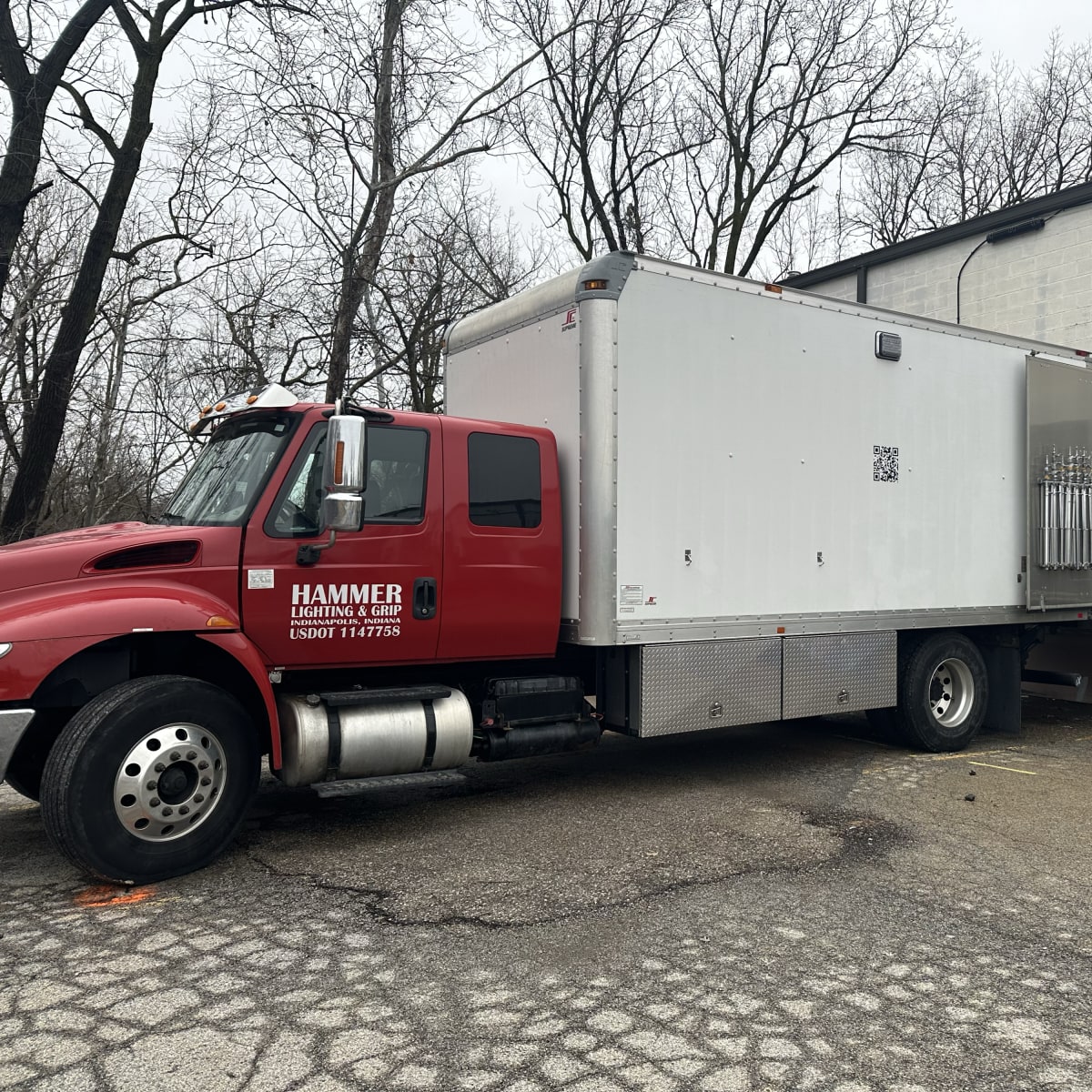 A red delivery truck is parked next to a loading dock of a white building, with equipment visible in the truck's back.