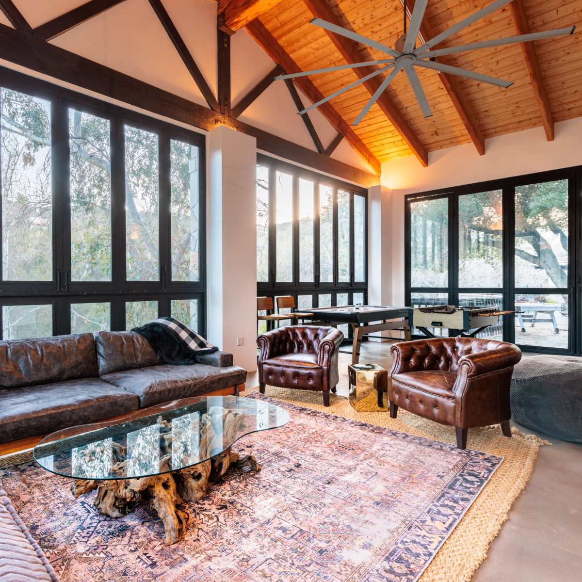 The living room features a large sectional sofa, two leather armchairs, a coffee table, and expansive windows that provide a view of the outdoors.