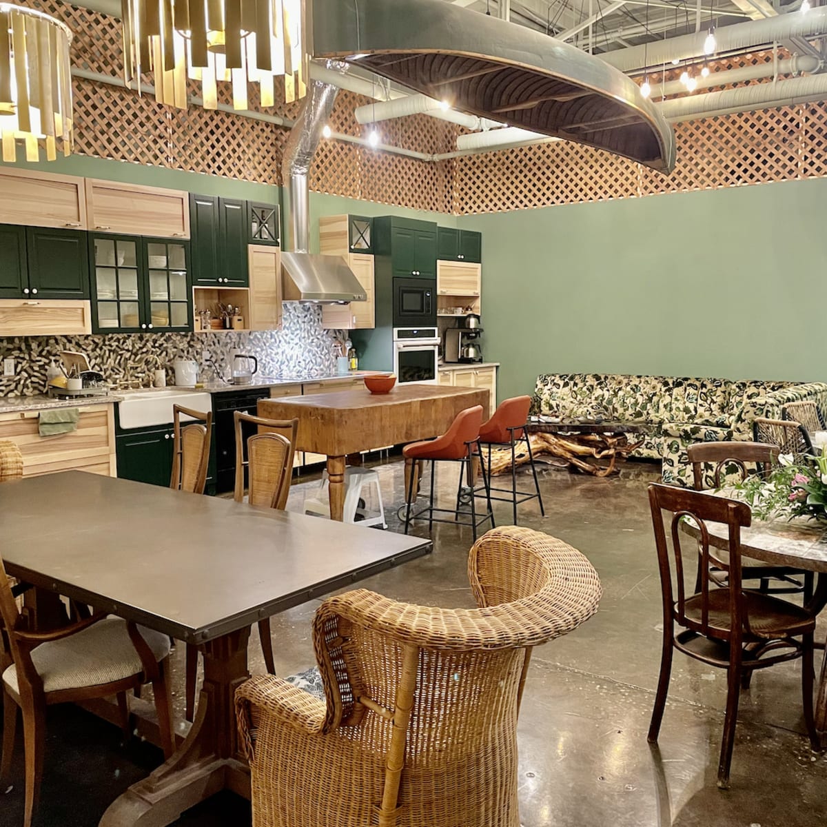 A spacious kitchen and dining area featuring modern furniture, a large table, and a colorful patterned sofa against a green wall.
