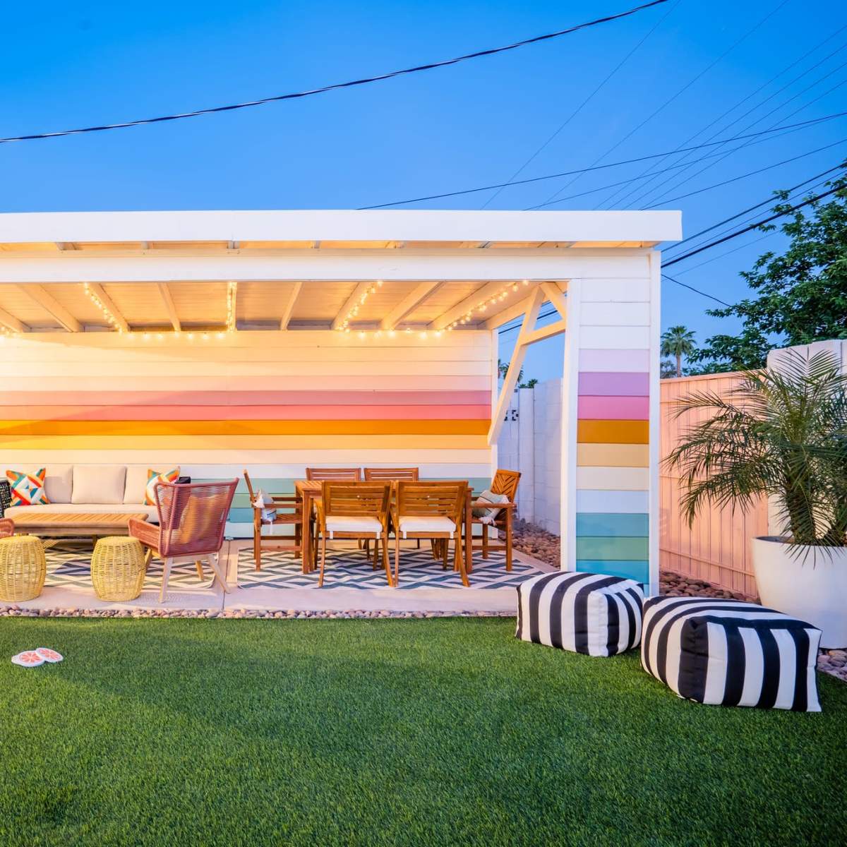 A brightly colored outdoor pavilion with comfortable seating, a dining area, and decorative elements surrounded by lush green grass and plants.