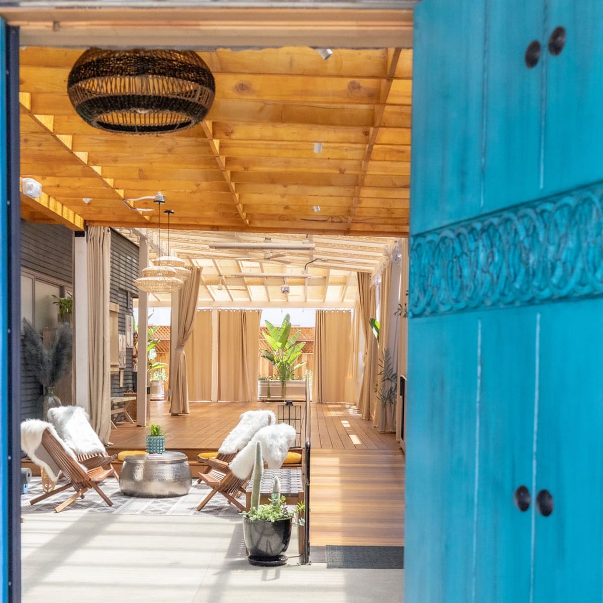 An open entrance leading into a spacious, well-lit indoor space with wooden beams, two lounge chairs, and plants.