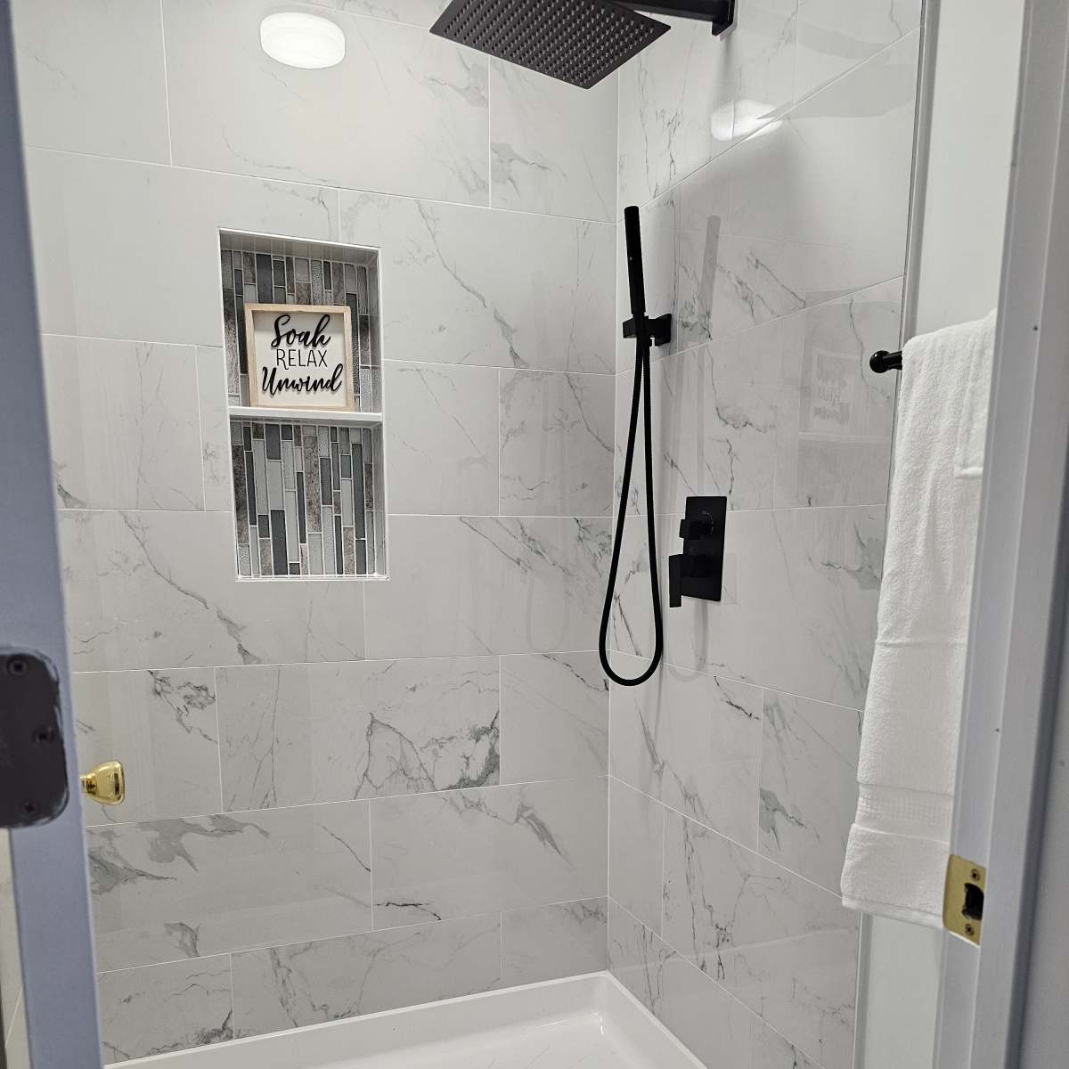A modern shower stall with white tiled walls, a rainfall showerhead, and a small decorative niche.