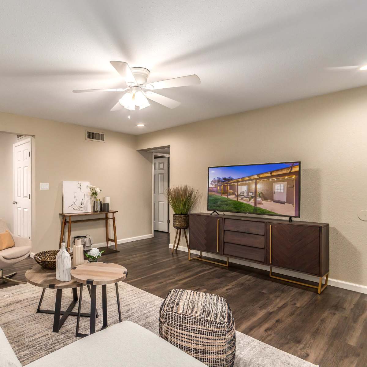 A cozy living room with a ceiling fan, a television on a cabinet, modern furniture, and a dining area visible in the background.