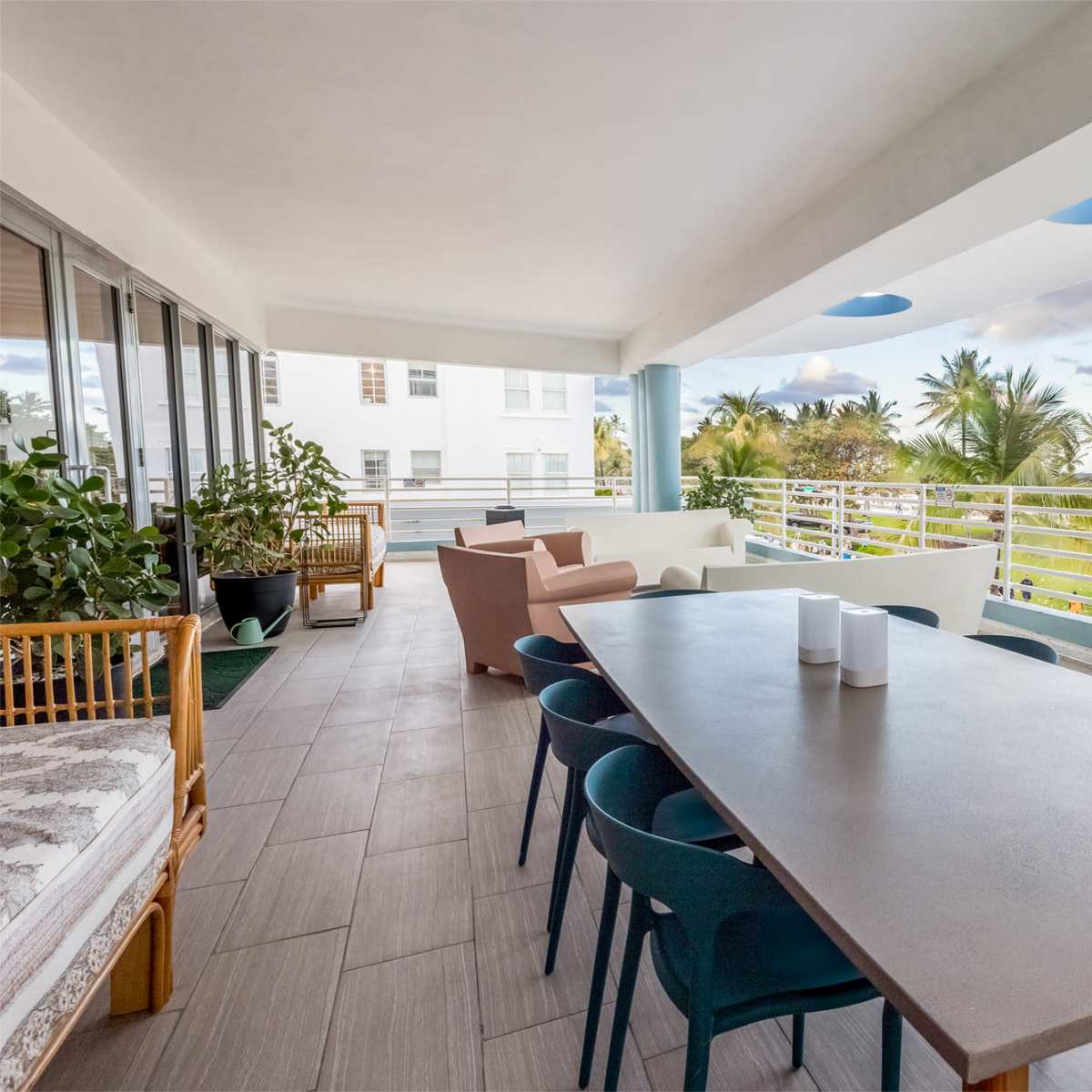 A spacious balcony with a long dining table surrounded by chairs, potted plants, and seating areas overlooking a lush landscape.