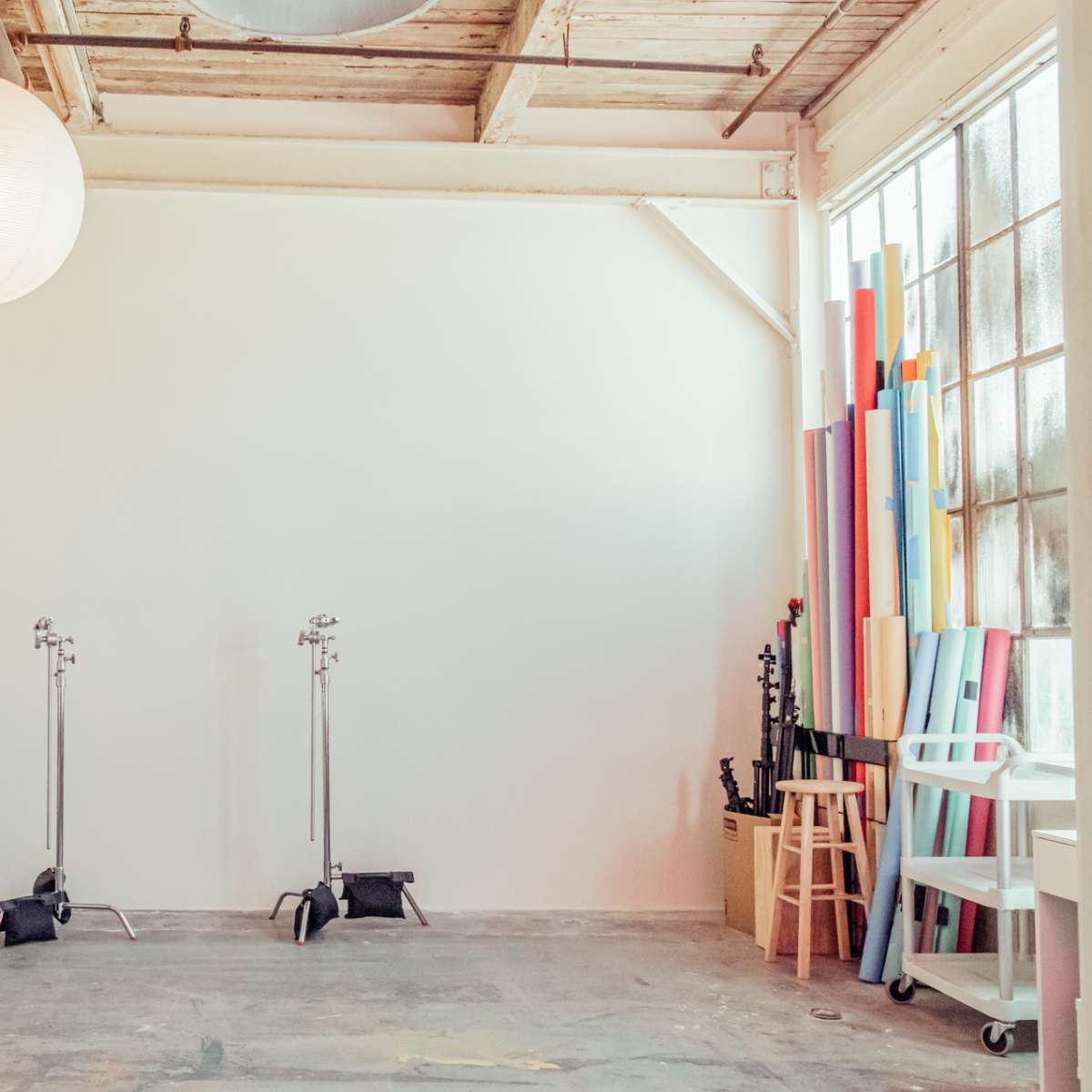 A spacious room with a white wall, a pink ladder, two light stands, colorful rolls of paper, and a couch in the corner.