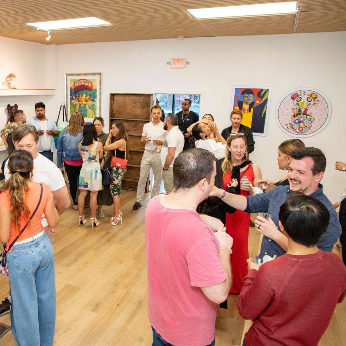 A group of people socialize and enjoy drinks at an event in a brightly lit art gallery.