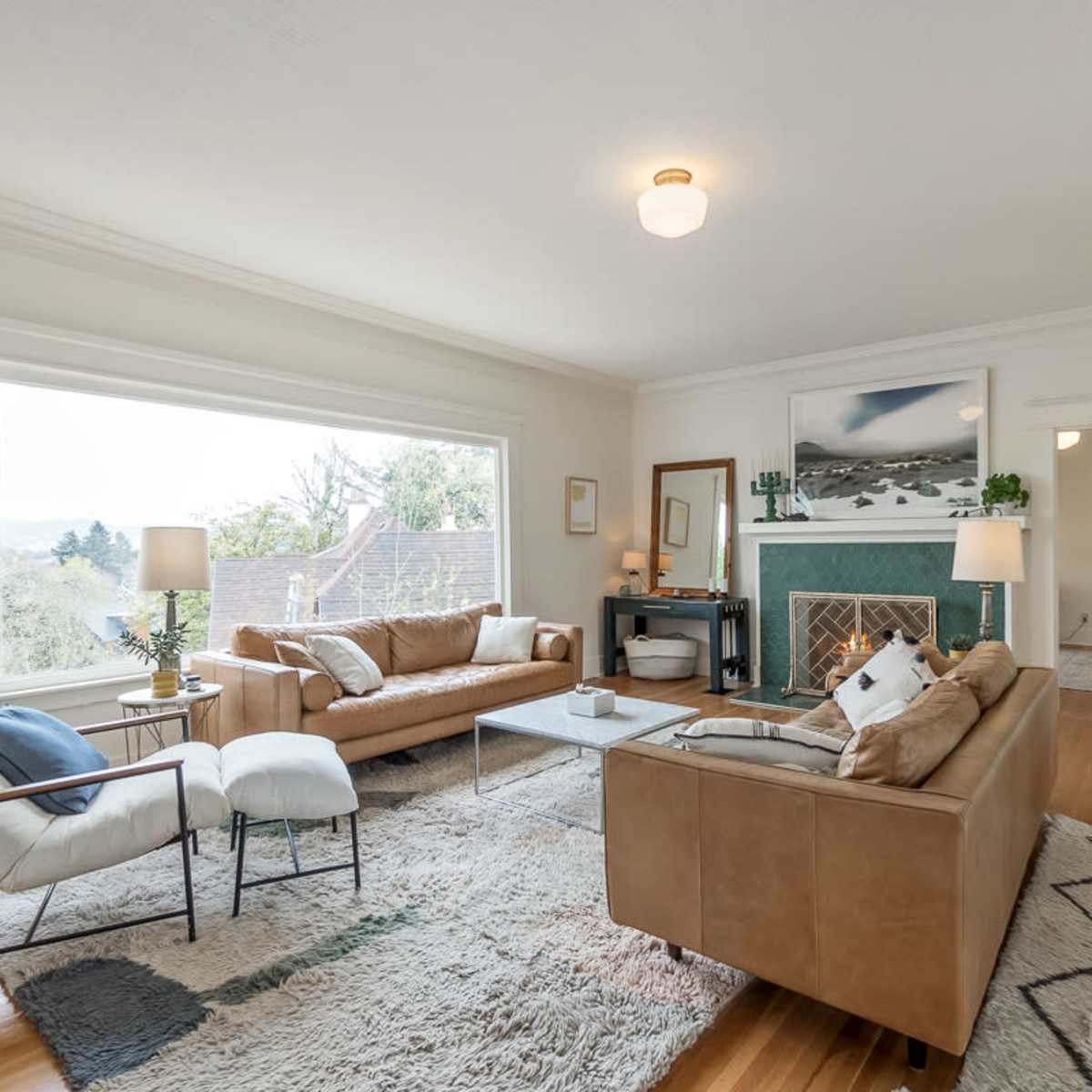 A spacious living room with large windows, two sofas, a coffee table, and a green fireplace, all arranged on a patterned rug.