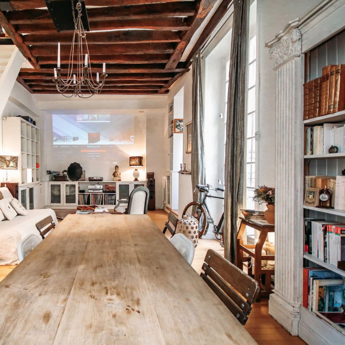 A modern living space with a wooden dining table, chairs, an open staircase, and shelves filled with books.