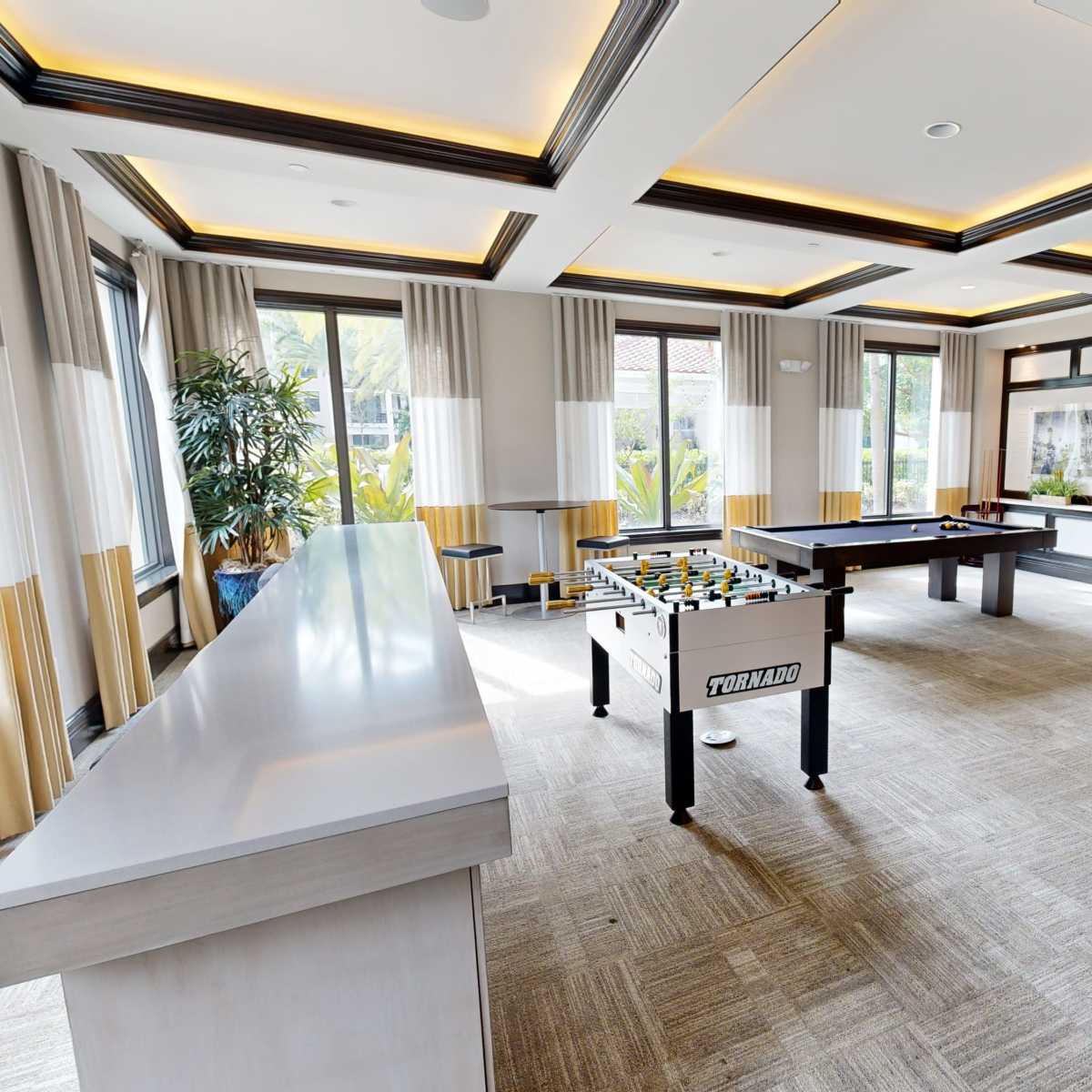 A spacious game room featuring a foosball table, a pool table, and a large television against the wall.