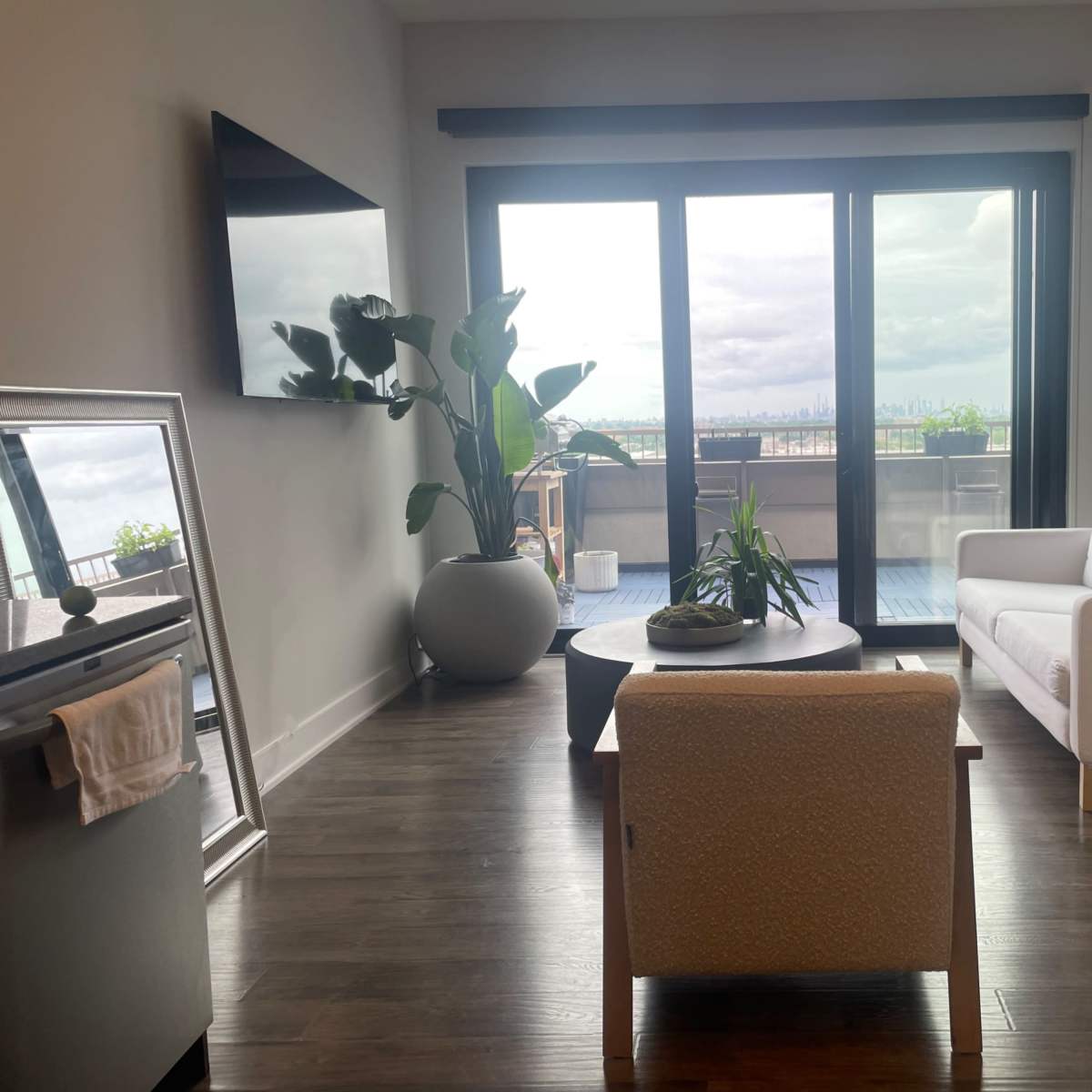 A modern living room features a white sofa, a round coffee table, and a large window with a city view.