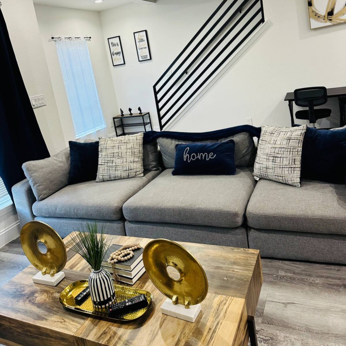 A modern living room with a gray sectional sofa, a wooden coffee table adorned with decorative items, and a staircase in the background.