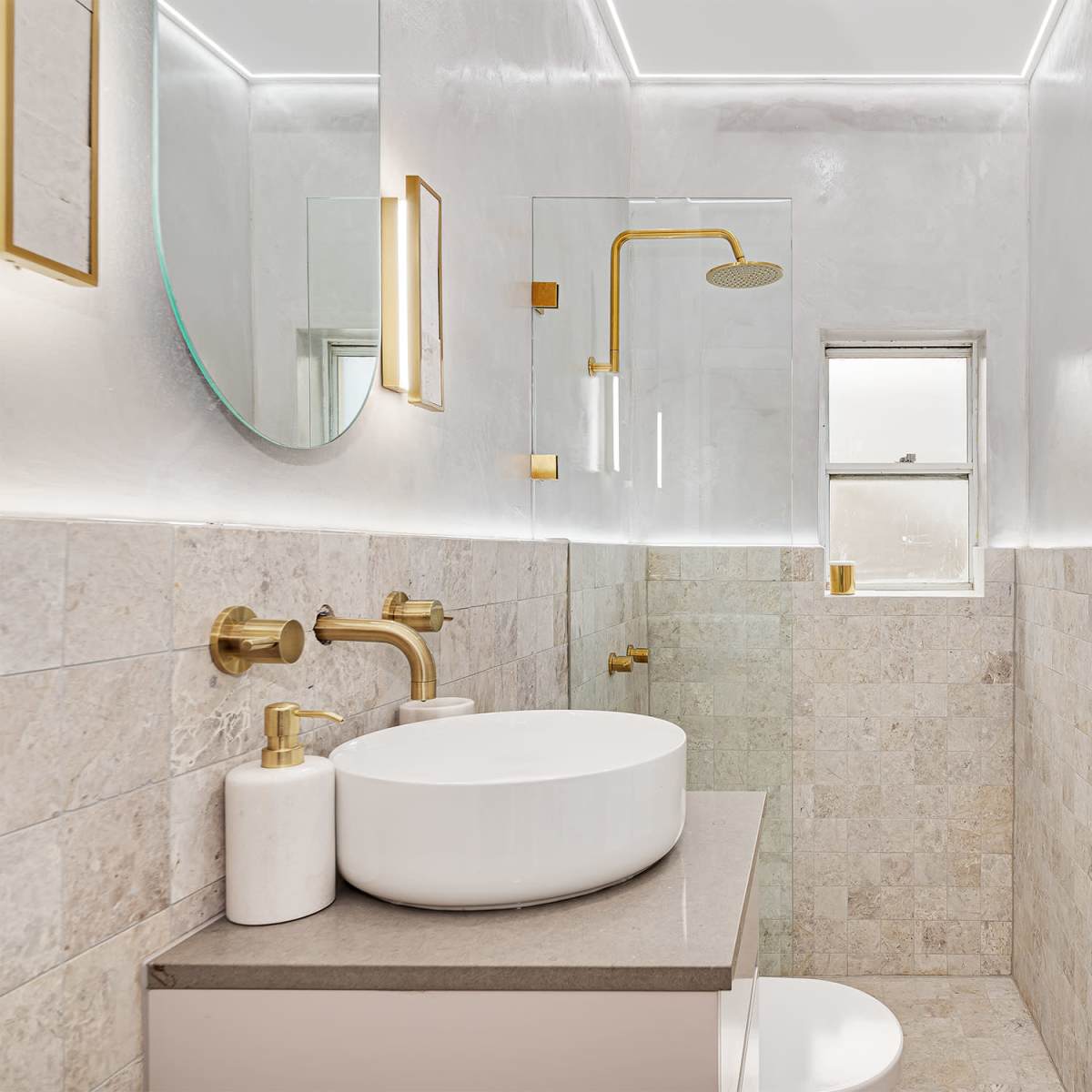 A modern bathroom with a shower, a circular mirror, a circular sink on a countertop, and beige tiled walls.
