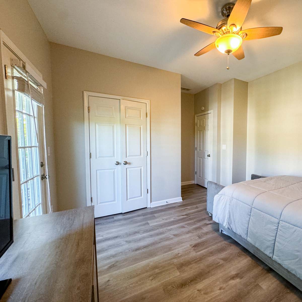 A bedroom with a bed, a ceiling fan, a television on a dresser, and two closed doors.
