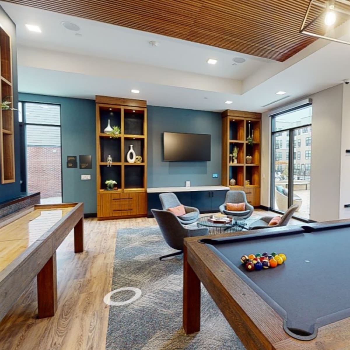 A modern recreational room with a billiard table, seating area, and large windows overlooking a garden.