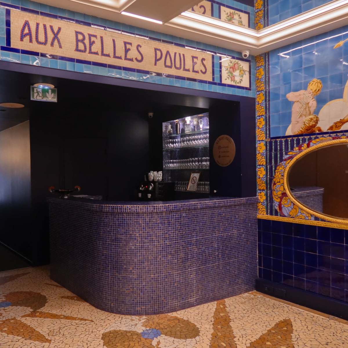 A tiled bar area with a mosaic floor and decorative wall tiles featuring a mirror and illustrations.