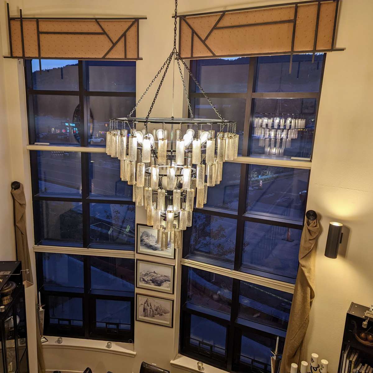 A well-lit interior with large windows, a modern chandelier hanging from the ceiling, and decorative items on the walls and shelves.