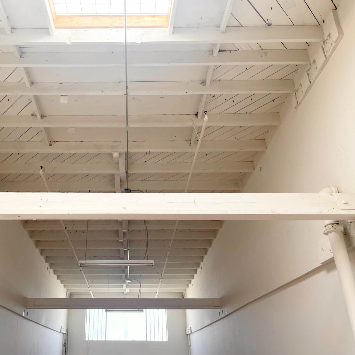 A bright interior space with high white wooden beams and a skylight, leading towards a distant wall with windows.