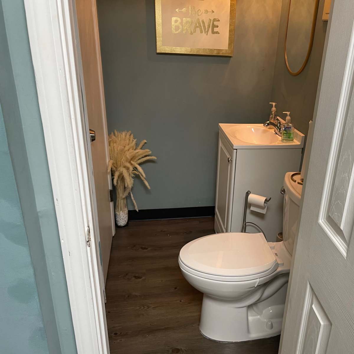 A small bathroom with a toilet, sink, and decorative wall art, accessible through a door.