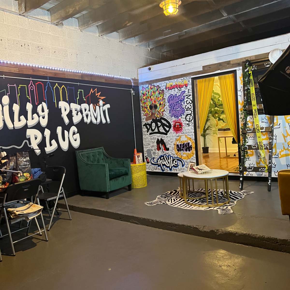 A colorful room with graffiti art on the walls, a green armchair, a coffee table on a patterned rug, and an area designed for casual gatherings or photo shoots.