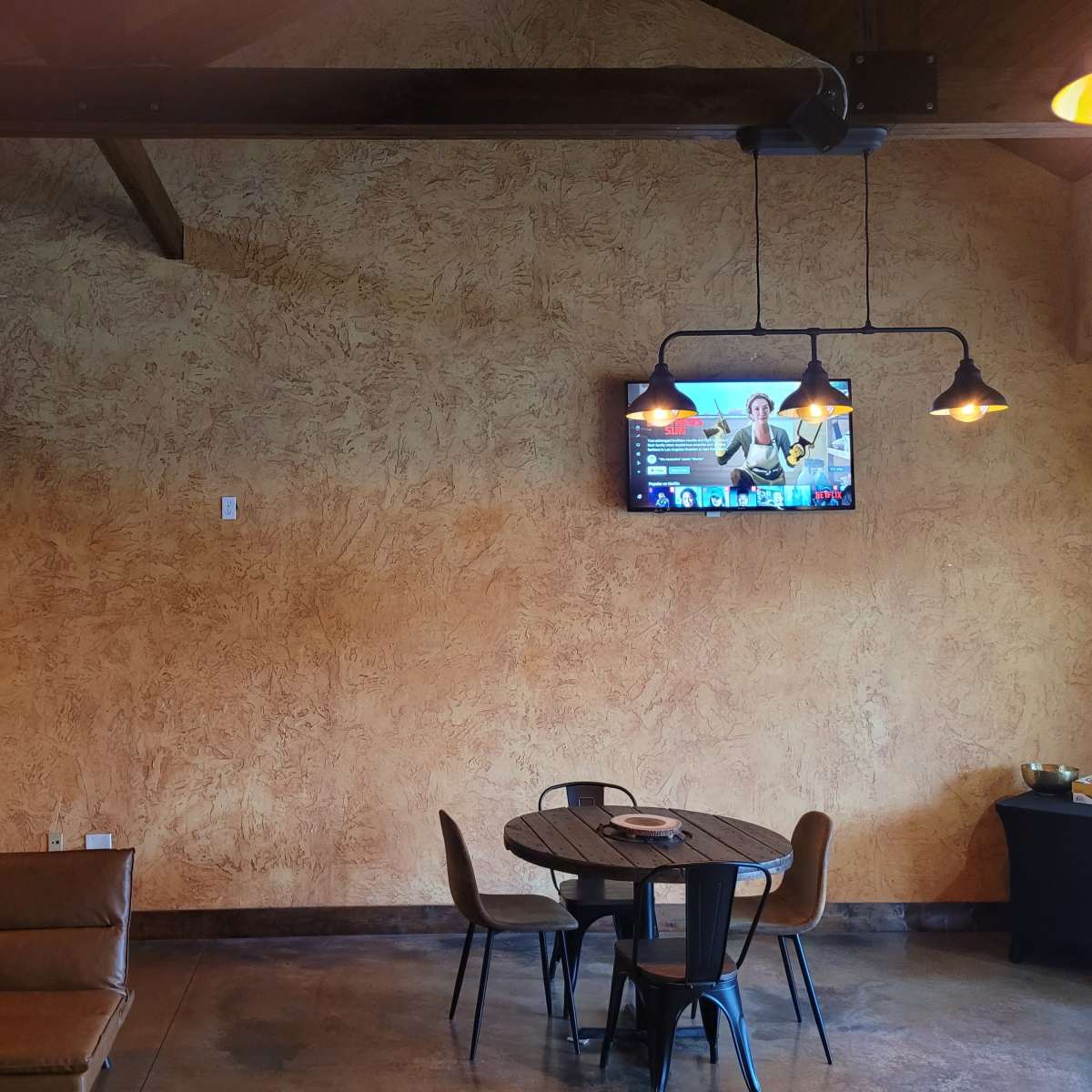 A textured wall with two mounted screens and a circular dining table surrounded by chairs.