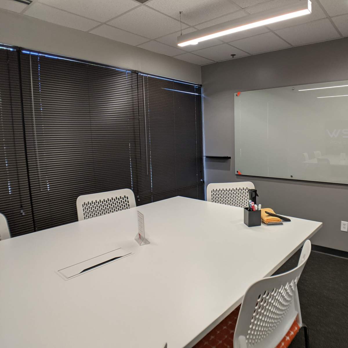 A conference room with a large white table, several white chairs, and a glass board on the wall.