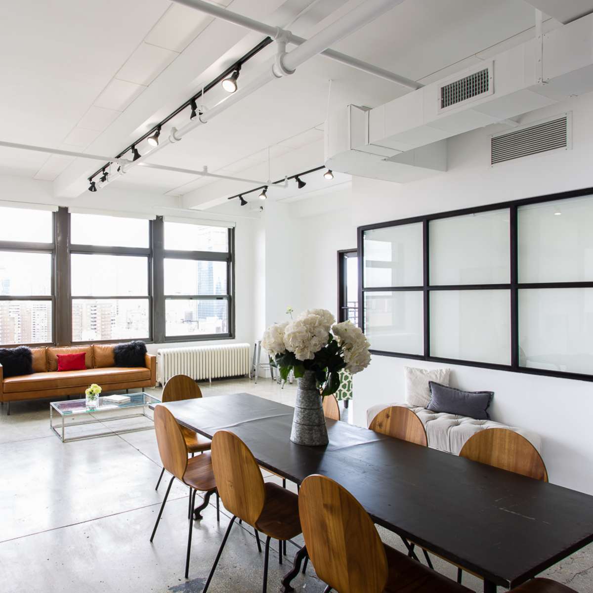 A modern living space featuring a dining table, a sofa, large windows with city views, and minimalistic decor.