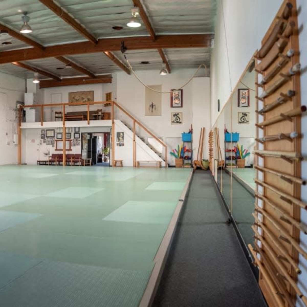 A spacious martial arts studio with tatami mats, wooden beams, and various wall decorations.