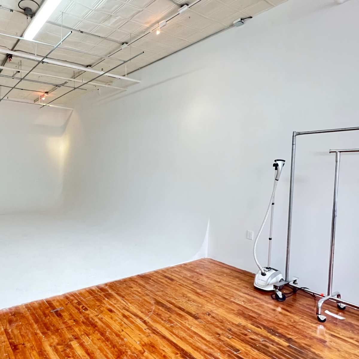A spacious photography studio featuring a seamless white backdrop and polished wooden flooring.
