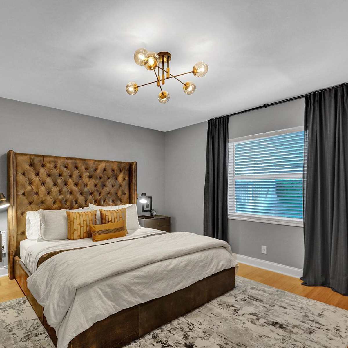 A modern bedroom featuring a tufted brown headboard, a bed with white bedding, two nightstands, and a window with gray curtains.